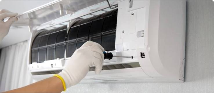 Gloved hands servicing a wall-mounted indoor air conditioning unit